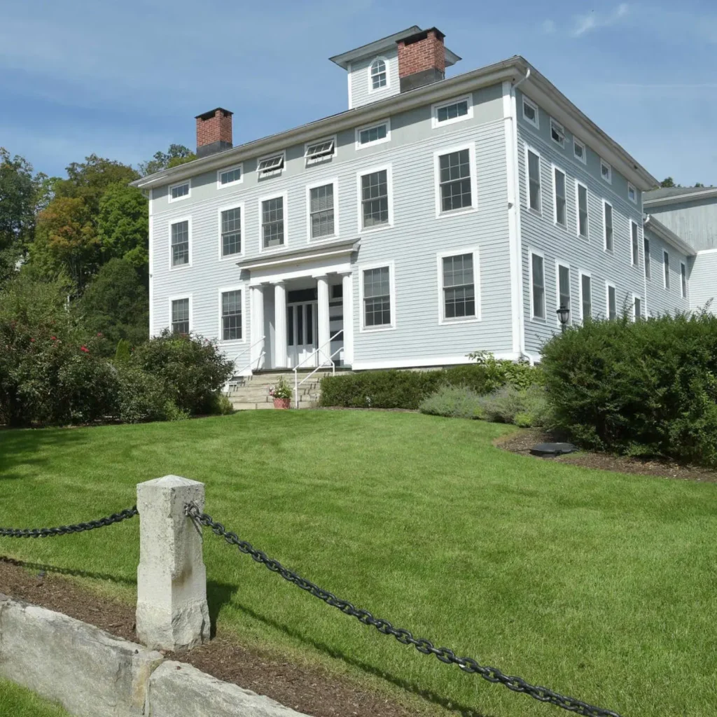 A stately light blue building surrounded by greenery, home to Old Glory Days' adult day care center in Sandy Hook, CT.